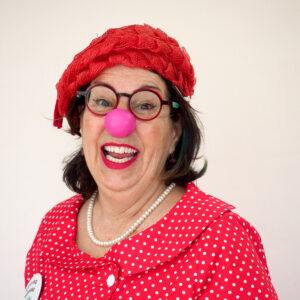 Femme clown souriante avec nez rouge et chapeau.