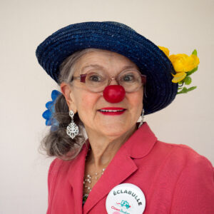 Femme clown souriante avec chapeau et nez rouge.