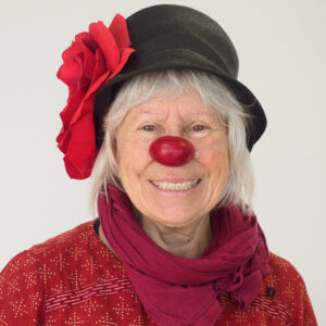 Personne souriante avec nez rouge et chapeau.