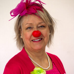Femme souriante avec tenue clown, nez rouge.