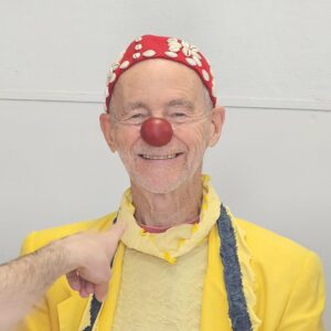 Clown souriant avec nez rouge et costume jaune.