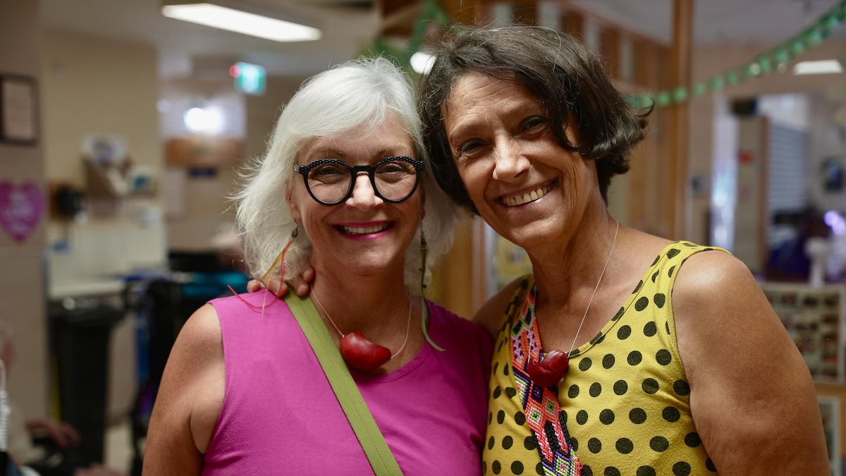 Deux femmes souriantes portant des colliers rouges.